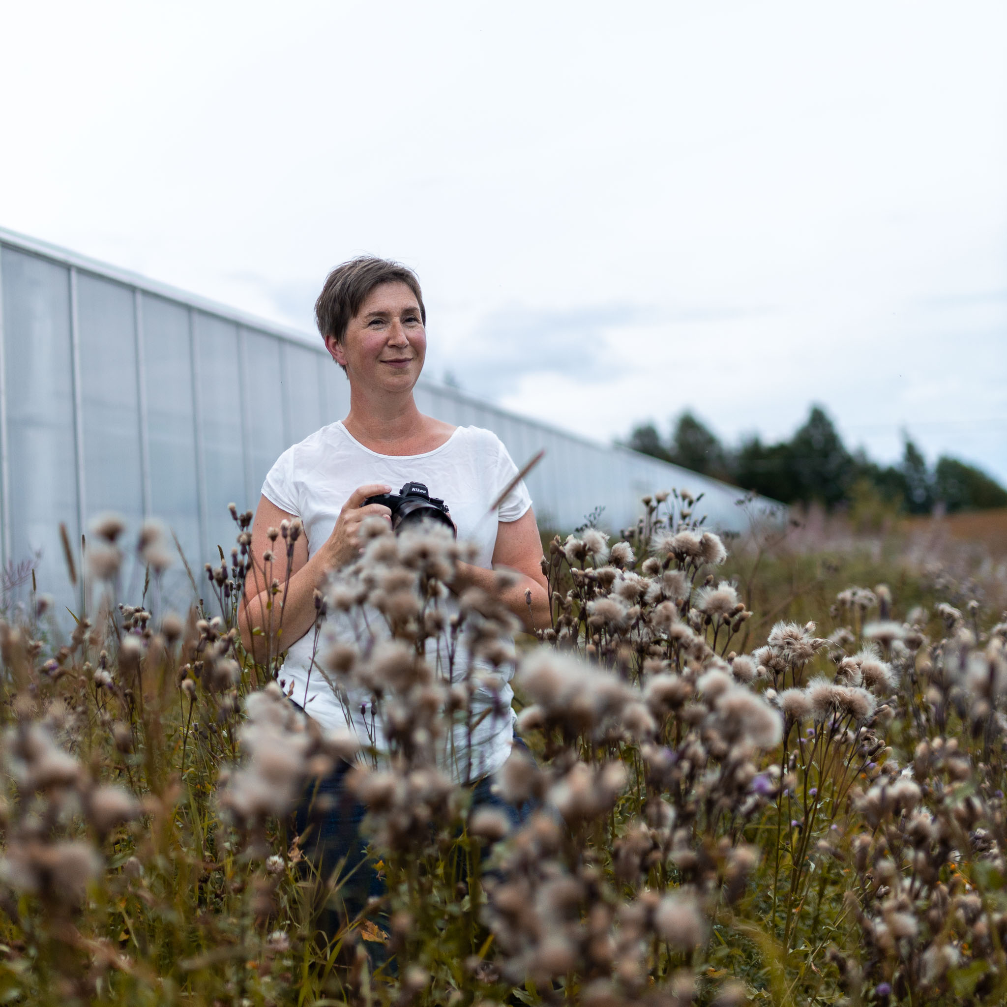 porträtt av en fotograf stående i ett fält av överblommade tistlar