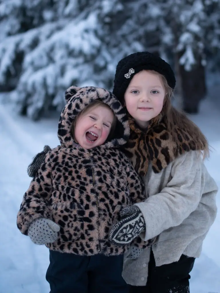 Två glada flickor i leopardmönstrade kläder står i snöig skog