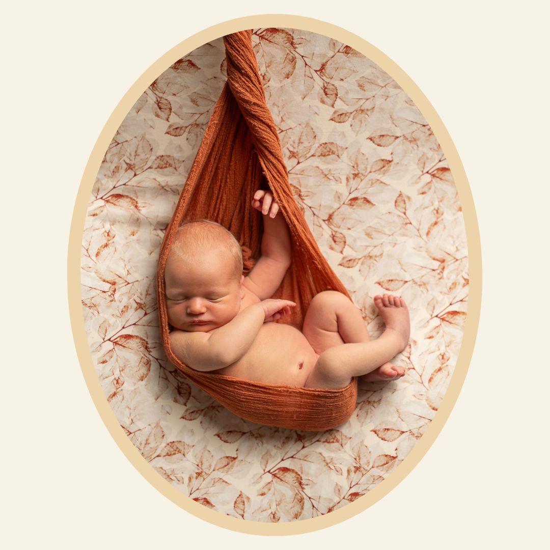 Nyfödd baby ligger poserad i ett rostrött tyg mot en beige och roströd bakgrund