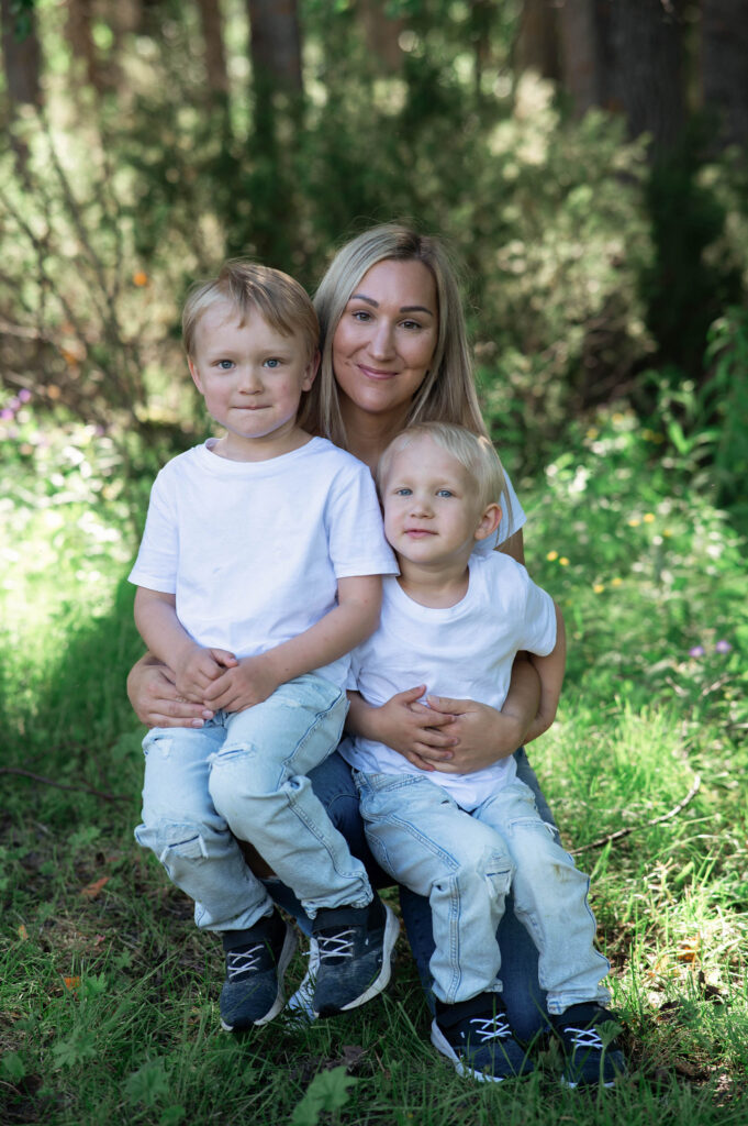 Två små pojkar sitter i knäet på sin mamma, alla tre är klädda i vit t-shirt och jeans