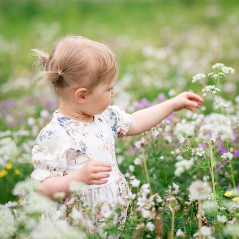 En liten flicka med pippilotter i håret står i en blomsteräng och känner på några hundkäx