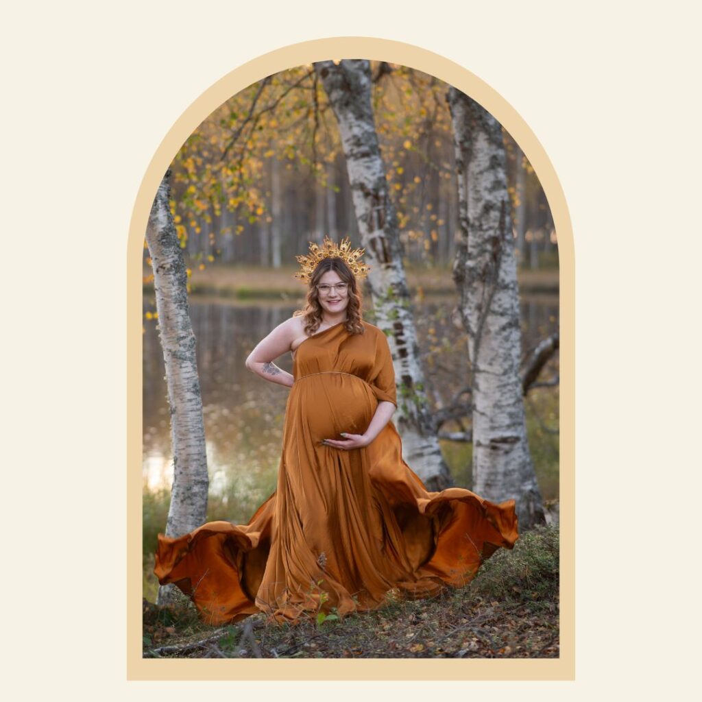 Gravid kvinna i gyllene klänning står i ett höstigt landskap.