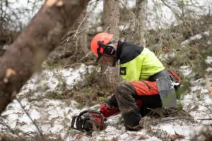 Man som tankar en husqvarna motorsåg. Mannen är klädd i skogshuggarkläder med hjäm och skyddsbyxor.