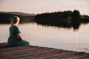 En kvinna sitter på en brygga vänd bort brån kameran. I bakgrunden syns solnedgång över Ångermanälven.