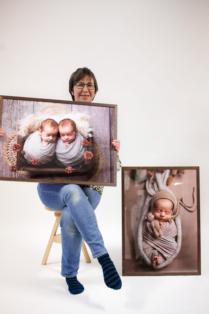 Fotografen Zandra Ahlqvist sitter på en pall och håller i en stor tavla av ett nyfött tvillingpar. Vid sidan står ett stativ med en lika stor tavla med en baby på.