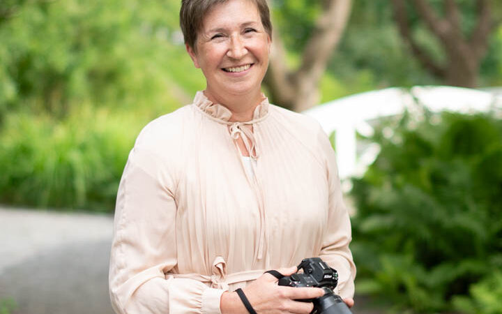 En leende kvinna tillika brandingfotograf tittar in i kamerna. I handen h&aring;ller hon sitt arbetsverktyg, en kamera