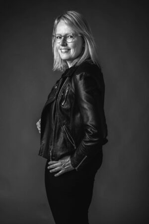 svartvitt prtr&auml;tt av kvinna i svarta jeans och skinnjacka, kvinnan ler avslappnat mot kameran